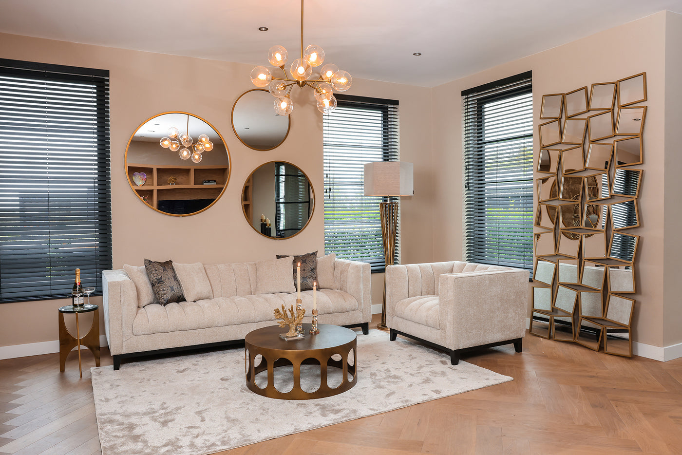Wohnzimmer mit cremefarbenes Sofa, Sessel und Teppich und dazu aus Gold Couchtisch mit Spiegeln und Hängelampe